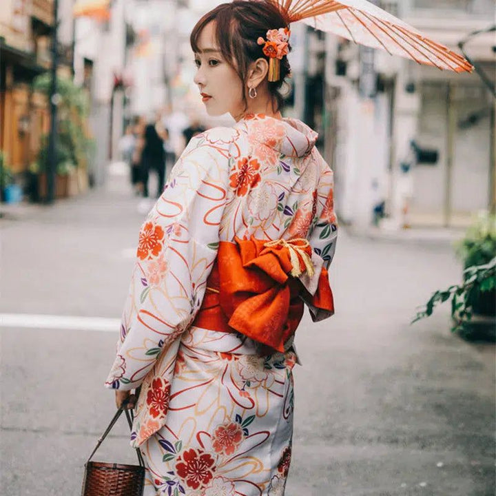 Femme portant un kimono fleuri blanc et orange, tenant une ombrelle. Découvrez notre collection de kimonos traditionnels japonais.