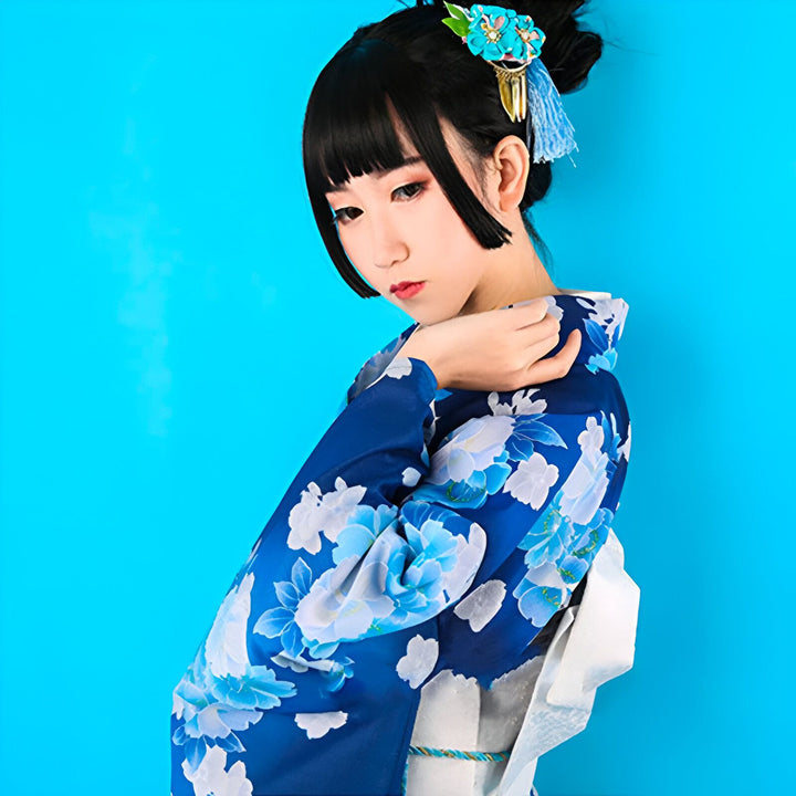 Jeune femme en kimono bleu à motifs floraux blancs, coiffure ornée d'une fleur bleue. Vêtements traditionnels japonais. Kimonos de haute qualité disponibles à l'achat. Découvrez notre collection de kimonos uniques.