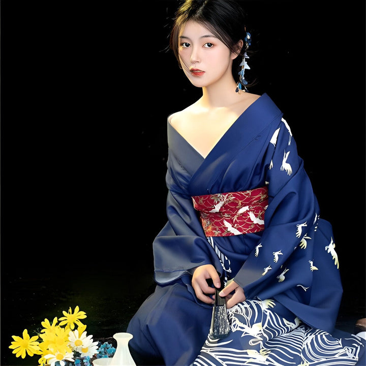 Femme en kimono bleu avec motifs de grues blanches et ceinture rouge ornée. Kimono traditionnel japonais en vente.