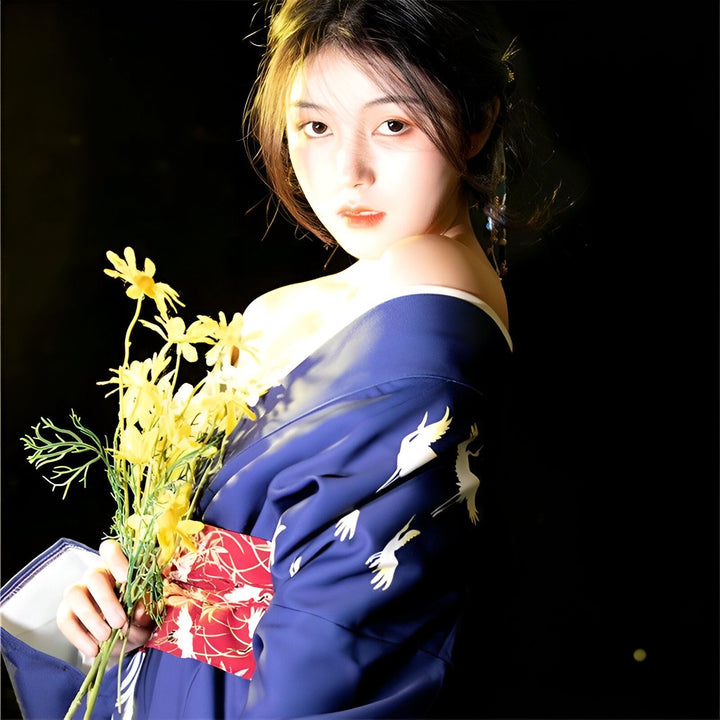 Jeune femme portant un kimono bleu orné de grues blanches, tenant un bouquet de fleurs jaunes. Kimonos élégants à vendre.