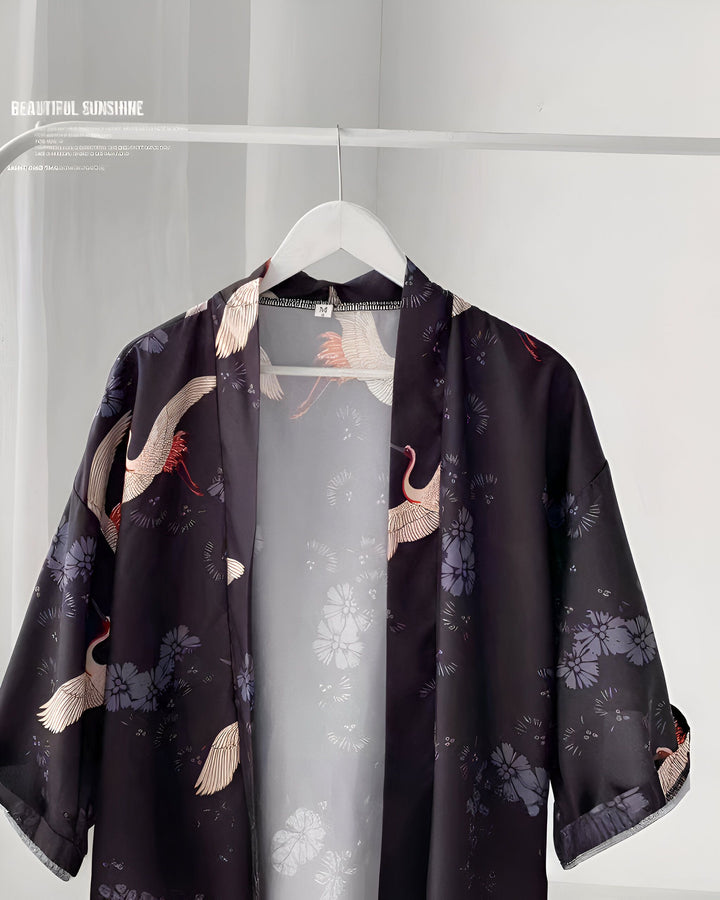 Kimono noir à motifs de grues et de fleurs, suspendu à un portant. Idéal pour un look japonais authentique. Découvrez notre collection de kimonos uniques.