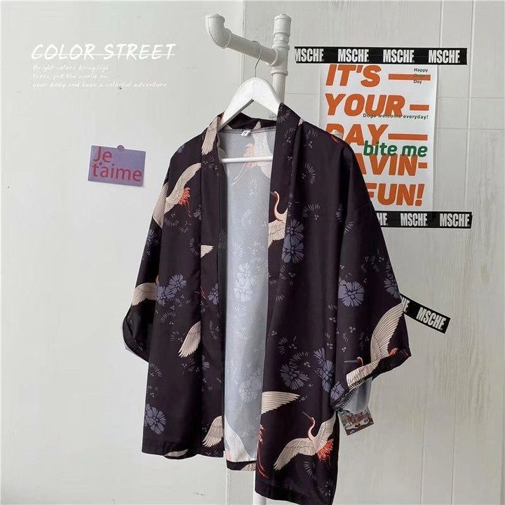 Kimono noir avec motifs de grues et de fleurs, suspendu sur un cintre. Vêtement de style japonais, idéal pour une tenue décontractée et élégante. Découvrez notre collection de kimonos uniques.