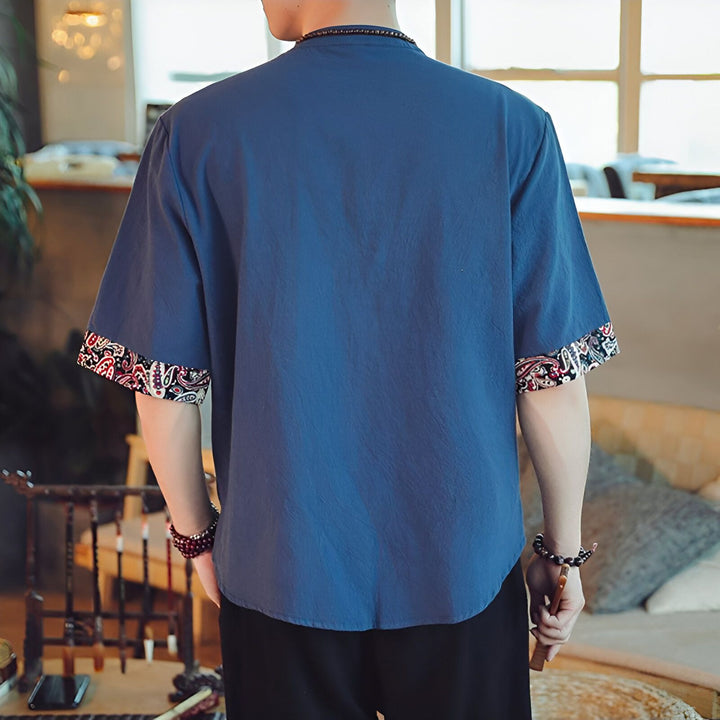 Vue arrière d'un homme portant une chemise bleue à manches courtes avec motifs ethniques aux poignets.