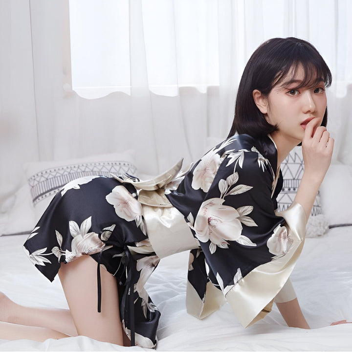 Femme portant un kimono noir à fleurs, assise sur un lit blanc. Kimono en satin avec ceinture assortie. Vêtements traditionnels japonais.