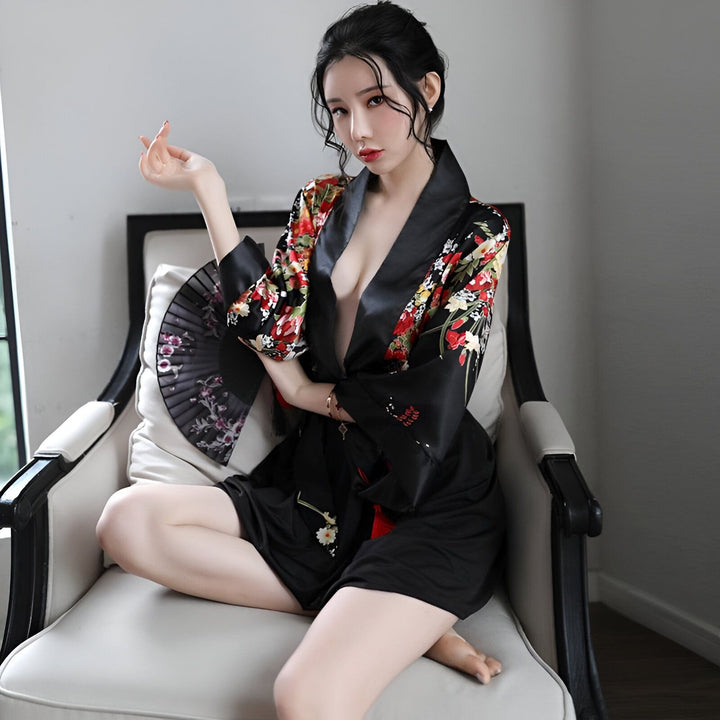 Femme assise portant un kimono noir court à motifs floraux colorés, tenant un éventail noir. Découvrez notre collection de kimonos pour femmes.