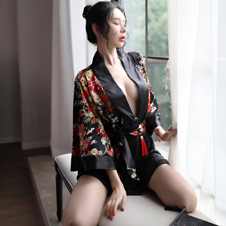 Femme assise portant un kimono noir à fleurs rouges, vertes et blanches. Kimono en satin avec ceinture, pour un look élégant et décontracté. Vêtements de nuit japonais disponibles à l'achat.