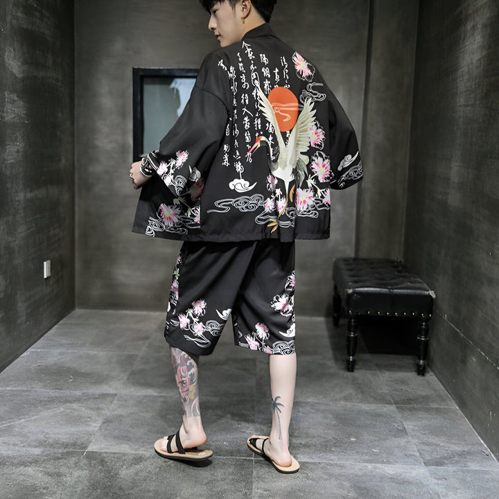 Homme portant un kimono noir avec un motif de grue blanche, fleurs roses et soleil rouge. Ensemble kimono et short assorti. Vêtements japonais traditionnels en vente.