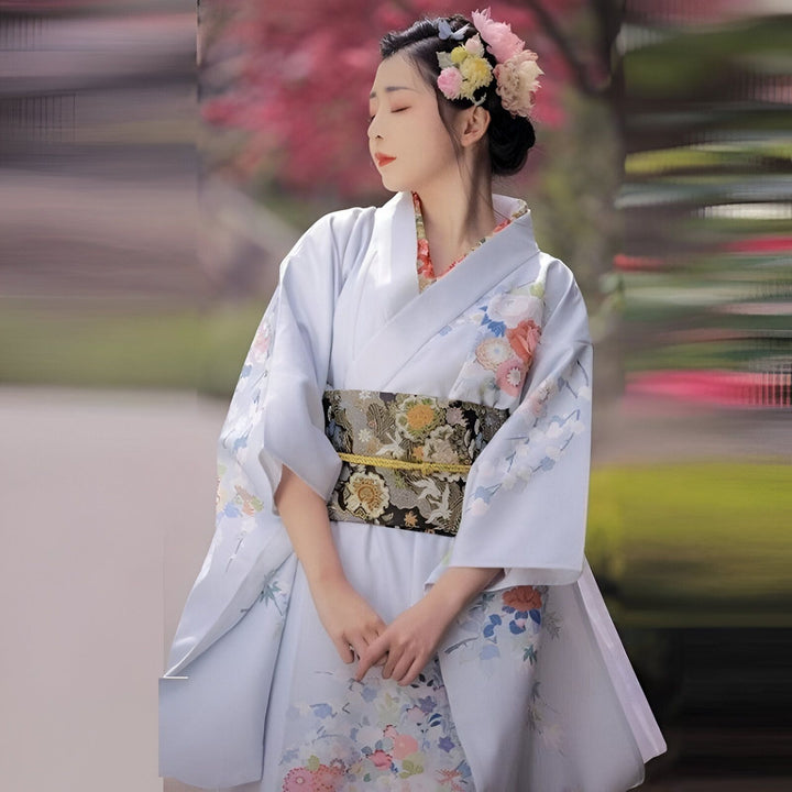 Femme portant un kimono traditionnel bleu clair avec des motifs floraux. Ceinture obi ornementale. Fleurs dans les cheveux. Kimonos authentiques en vente.