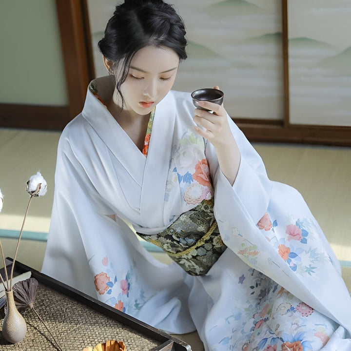 Femme portant un kimono blanc fleuri, assise sur un tatami, tenant une tasse de thé. Vêtements traditionnels japonais. Kimonos de qualité supérieure à vendre en ligne.