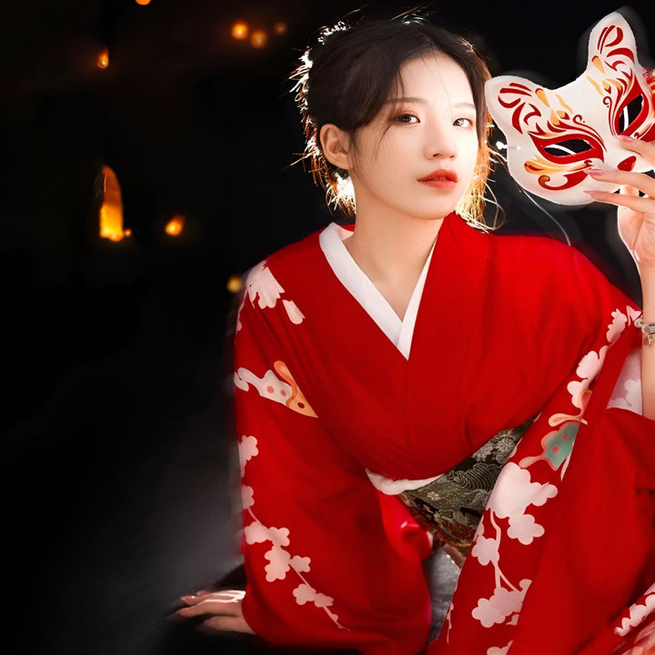 Femme en kimono rouge avec motif floral, tenant un masque de renard blanc et rouge. Vente de kimonos traditionnels et modernes.