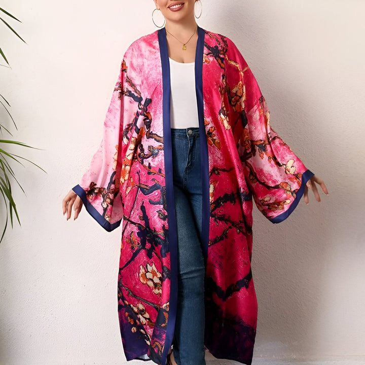 Femme souriante portant un kimono long rose vif avec des motifs floraux bleus et noirs, idéal pour une tenue décontractée et élégante. Kimono de notre collection.