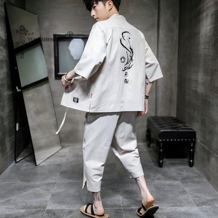 Homme portant un kimono beige avec un motif de poisson et des caractères japonais sur le dos, pantalon assorti et sandales. Vente de kimonos en ligne.