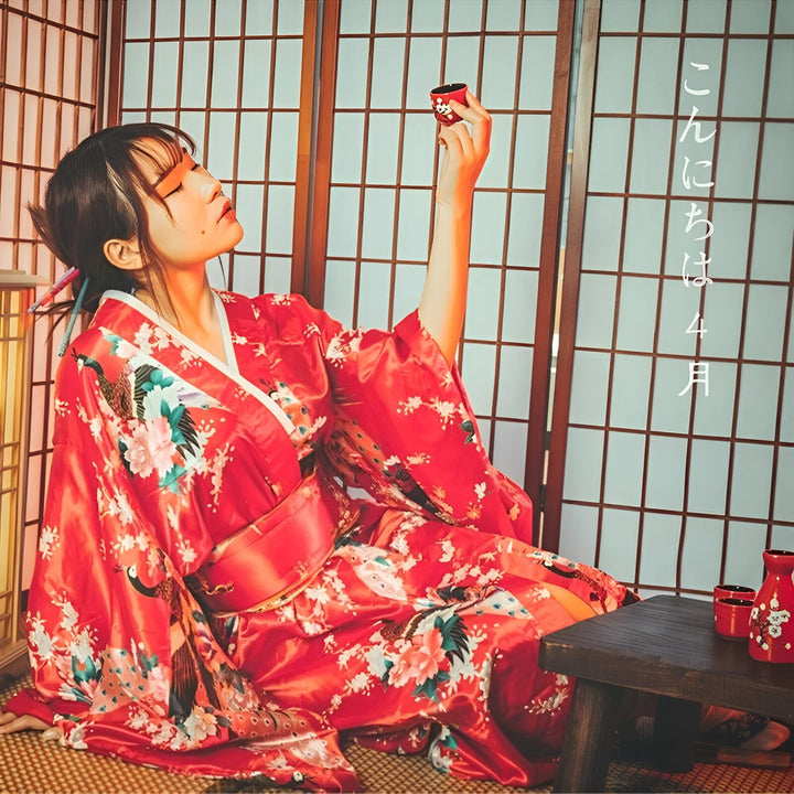Femme en kimono rouge fleuri tenant une tasse de saké. Vente de kimonos traditionnels japonais.