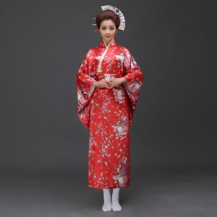 Femme portant un kimono rouge traditionnel avec motifs floraux, coiffure et maquillage de geisha, éventail décoratif. Kimonos authentiques à vendre.