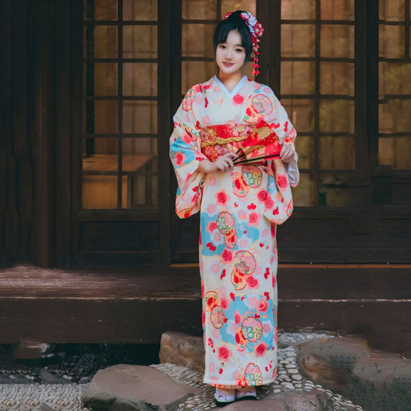 Jeune femme souriante portant un kimono traditionnel japonais à motifs floraux. Elle tient un éventail rouge. Kimono disponible à l'achat.