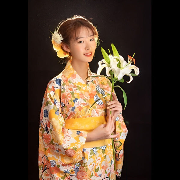 Jeune femme souriante portant un kimono japonais jaune fleuri et tenant un lys blanc. Vêtements traditionnels japonais en vente.