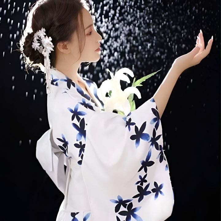Femme portant un kimono blanc à motifs floraux bleus, coiffure ornée, tenant des fleurs blanches. Vente de kimonos traditionnels japonais et accessoires.