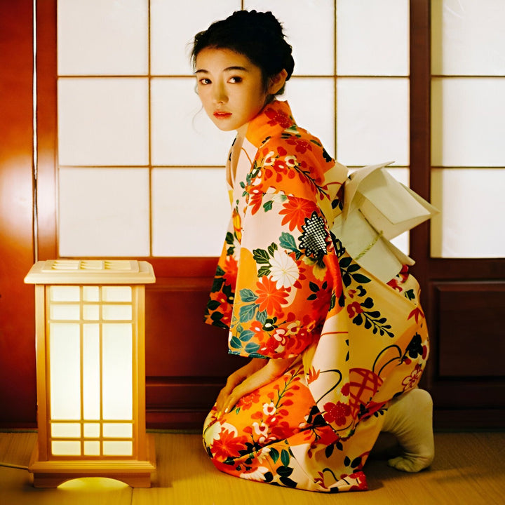 Femme en kimono floral orange et beige près d'une lanterne japonaise. Vente de kimonos traditionnels et modernes. Élégance et style japonais.