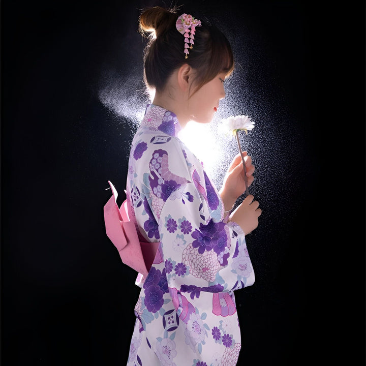 Femme en kimono traditionnel japonais à motifs floraux violets. Coiffure ornée, tenant une fleur blanche. Vente de kimonos authentiques.