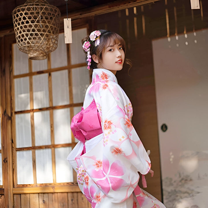 Jeune femme portant un kimono blanc à motifs floraux roses avec une ceinture obi rose. Vente de kimonos traditionnels japonais et accessoires. Découvrez notre collection unique de kimonos pour femmes.