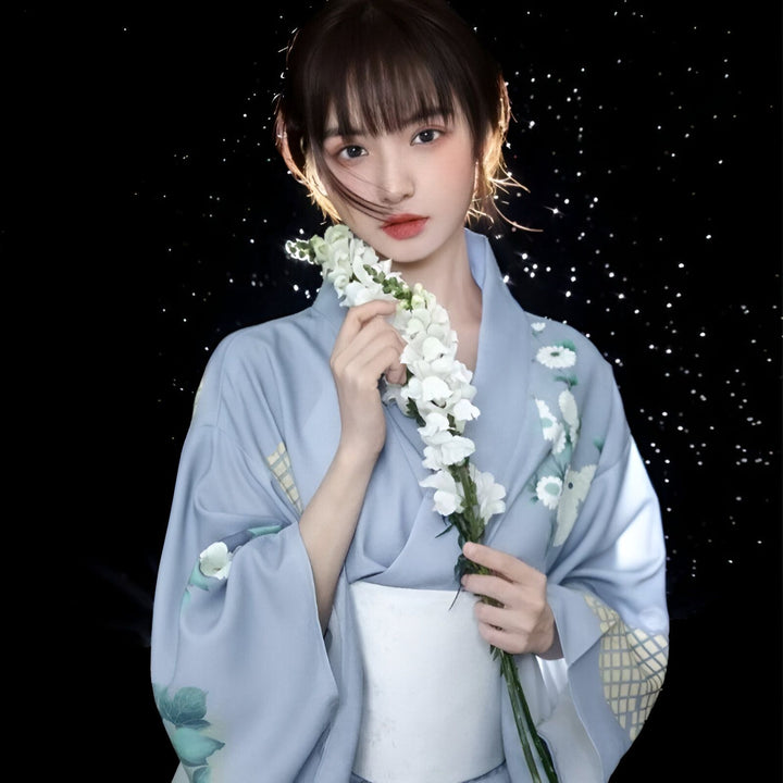 Jeune femme portant un kimono bleu clair avec motifs floraux blancs, tenant des fleurs blanches. Vêtements traditionnels japonais. Découvrez notre collection de kimonos.