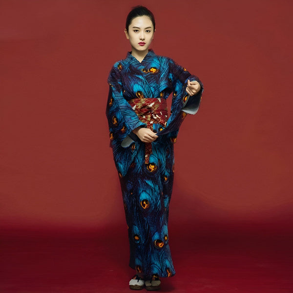 Femme portant un kimono bleu à motif de plumes de paon avec une ceinture obi rouge. Vêtements traditionnels japonais à vendre.