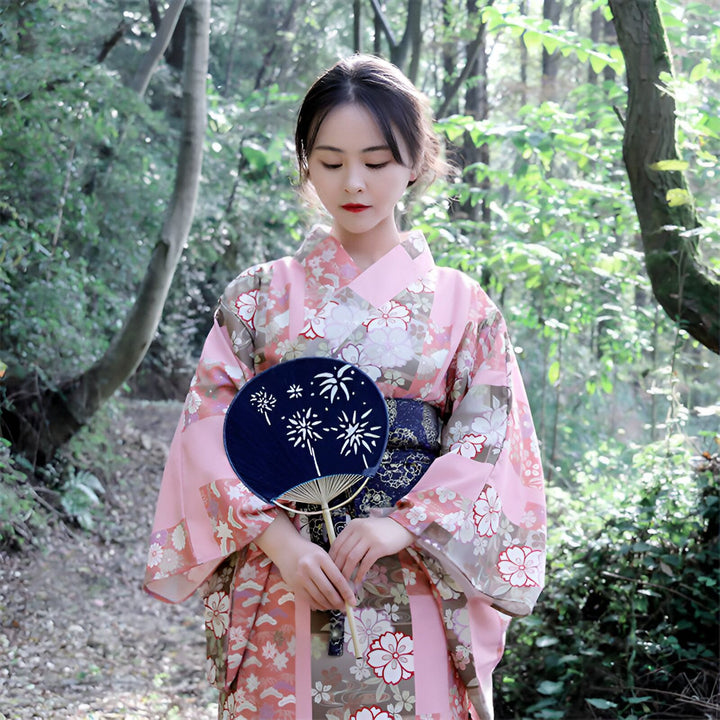 Femme portant un kimono rose à motifs floraux, tenant un éventail. Kimonos traditionnels japonais à vendre.