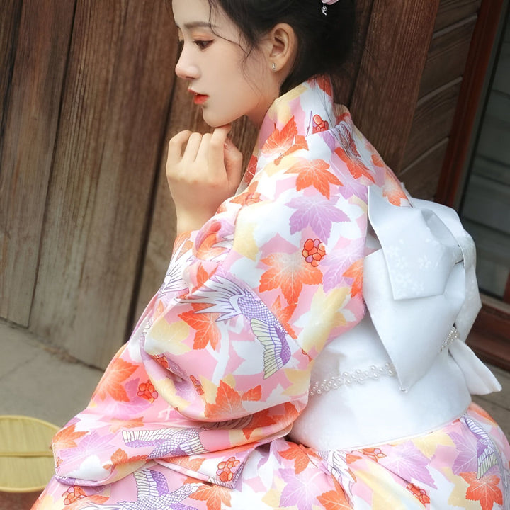Jeune femme portant un kimono traditionnel fleuri rose et orange. Vente de kimonos japonais authentiques en ligne. Motifs d'érable et d'oiseaux. Élégance et tradition japonaises.