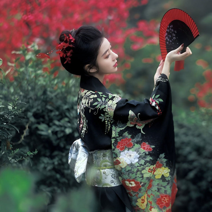Femme en kimono noir fleuri, tenant un éventail rouge et noir. Élégance japonaise, mode traditionnelle, vente de kimonos authentiques.