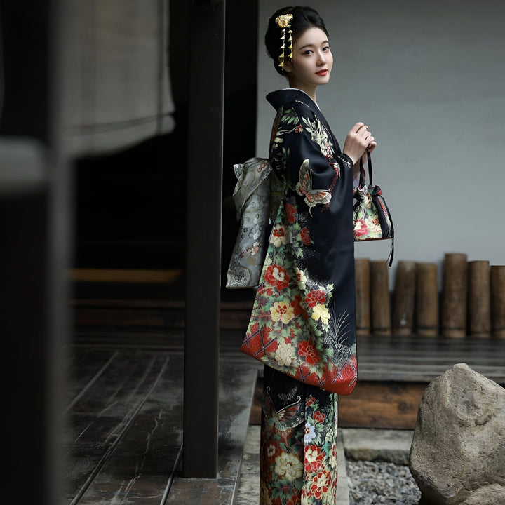 Femme portant un kimono noir orné de motifs floraux et de papillons. Elle tient un petit sac assorti. Vêtements traditionnels japonais. Kimonos en vente.