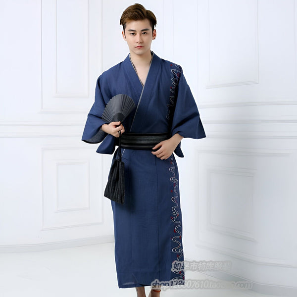 Homme portant un kimono bleu traditionnel avec une ceinture obi noire, tenant un éventail. Vêtements japonais élégants, parfaits pour la détente ou les événements spéciaux. Découvrez notre collection de kimonos pour hommes.
