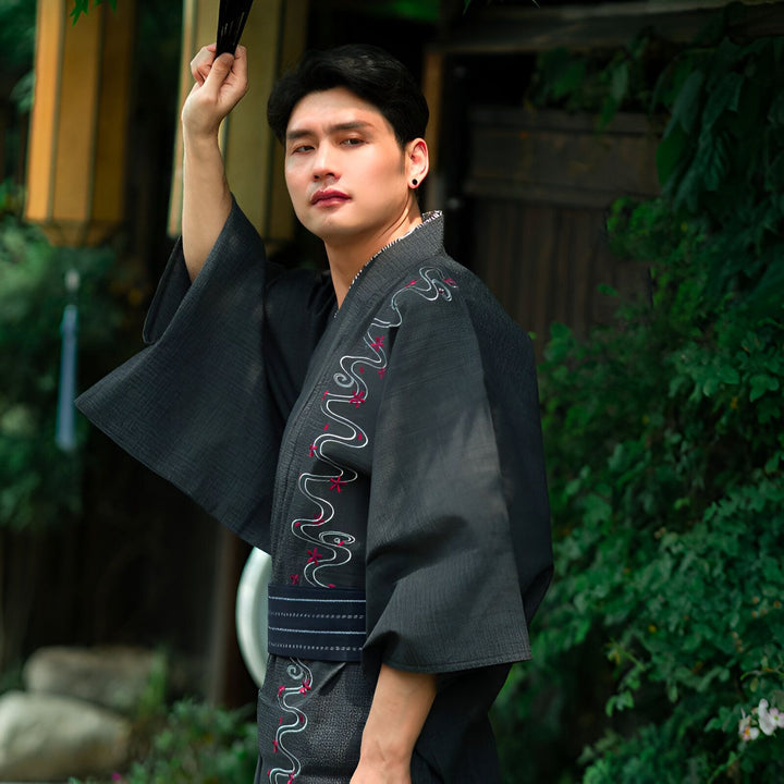 Homme portant un kimono japonais noir avec des motifs brodés blancs et rouges, tenant un éventail. Vêtements traditionnels, style asiatique. Kimonos à vendre.