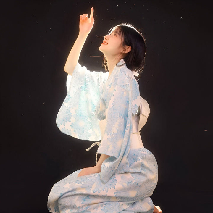 Jeune femme portant un kimono bleu à motifs floraux, pointant du doigt vers le ciel. Découvrez notre collection de kimonos traditionnels et modernes.