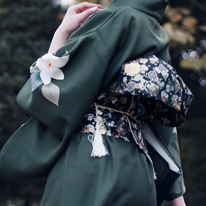 Dos d'une femme portant un kimono vert foncé avec motif floral blanc sur la manche et un obi à motifs floraux complexes. Kimono japonais traditionnel. Vêtements japonais en vente.