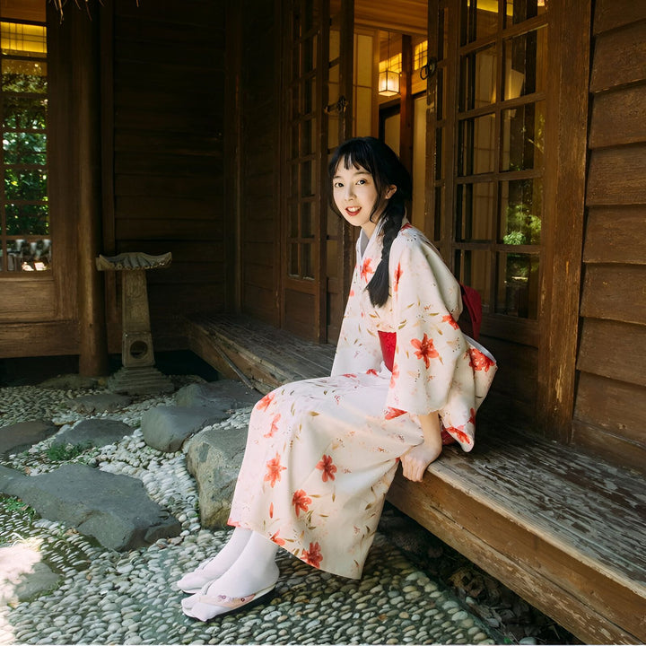 Femme souriante en kimono floral à l'extérieur d'une maison traditionnelle en bois. Découvrez nos kimonos uniques et élégants.