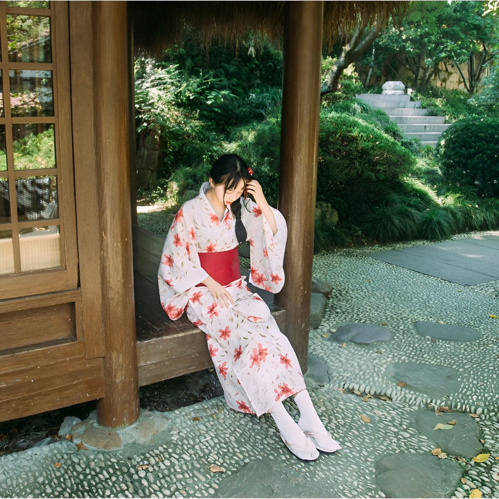 Femme portant un kimono fleuri avec une ceinture rouge, assise dans un jardin japonais. Vente de kimonos traditionnels et modernes.