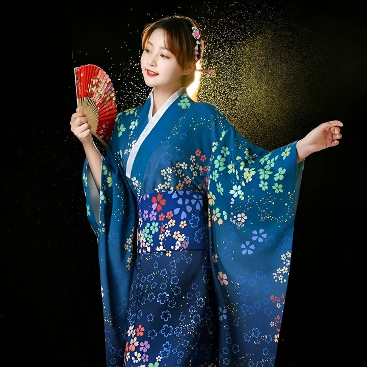 Femme souriante en kimono bleu à motifs floraux, tenant un éventail rouge. Kimonos traditionnels japonais à vendre.
