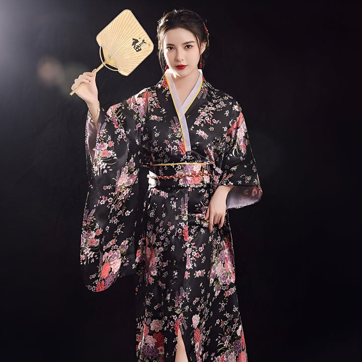 Femme portant un kimono noir à motifs floraux, tenant un éventail. Kimonos traditionnels et modernes à vendre.