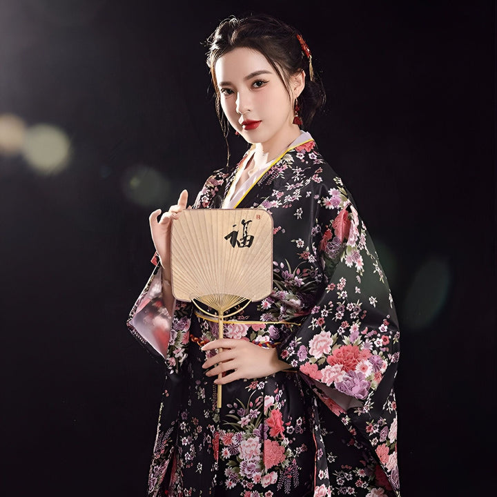 Femme portant un kimono floral noir et rouge, tenant un éventail. Kimonos traditionnels japonais à vendre. Élégance et style japonais. Découvrez notre collection de kimonos uniques.