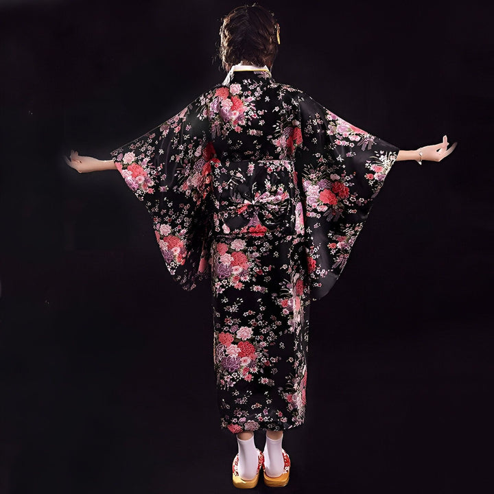 Femme de dos portant un kimono noir à motifs floraux rouges et roses. Vente de kimonos traditionnels japonais, yukata et accessoires assortis. Élégance et raffinement du Japon.