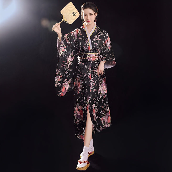 Femme en kimono noir à motifs floraux avec éventail, sandales traditionnelles. Vente de kimonos japonais authentiques.
