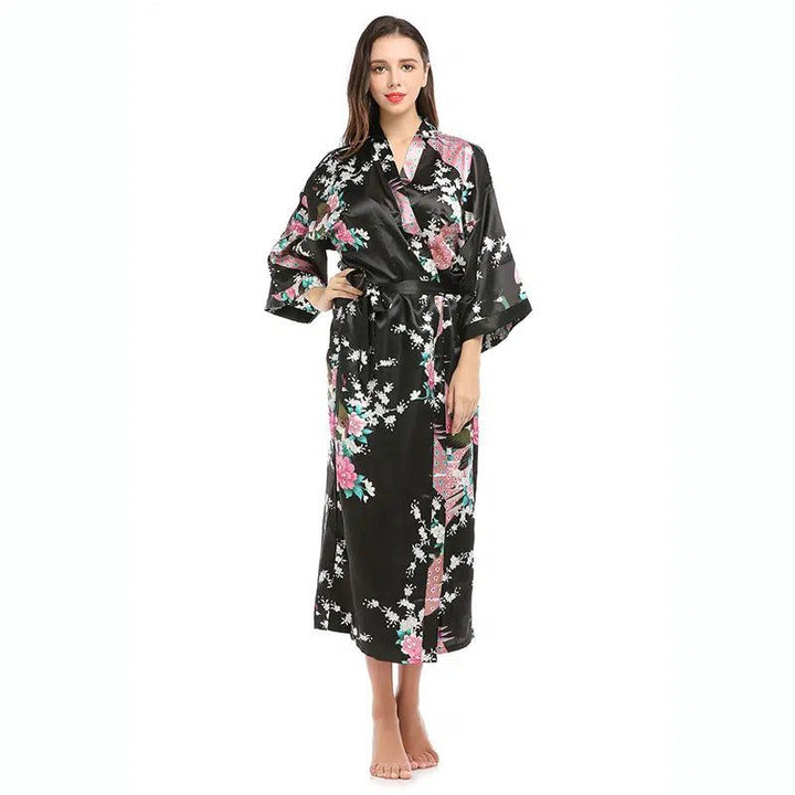 Femme portant un kimono long noir avec motifs floraux roses et blancs. Kimono de notre collection, idéal pour se détendre avec style. Découvrez nos kimonos.