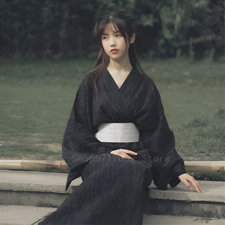 Jeune femme portant un kimono noir avec des rayures blanches. Élégance japonaise. Découvrez notre collection de kimonos uniques.