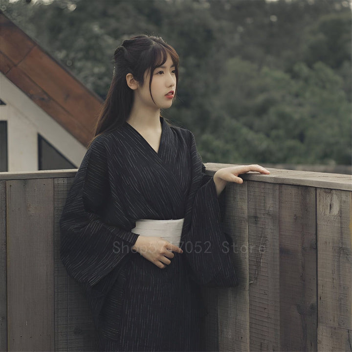 Jeune femme portant un kimono traditionnel japonais à rayures sombres et une ceinture blanche obi. Mode kimono japonais. Vêtements traditionnels japonais.