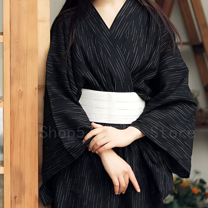 Femme portant un kimono noir à rayures blanches et une ceinture obi blanche. Kimono japonais traditionnel disponible à l'achat.