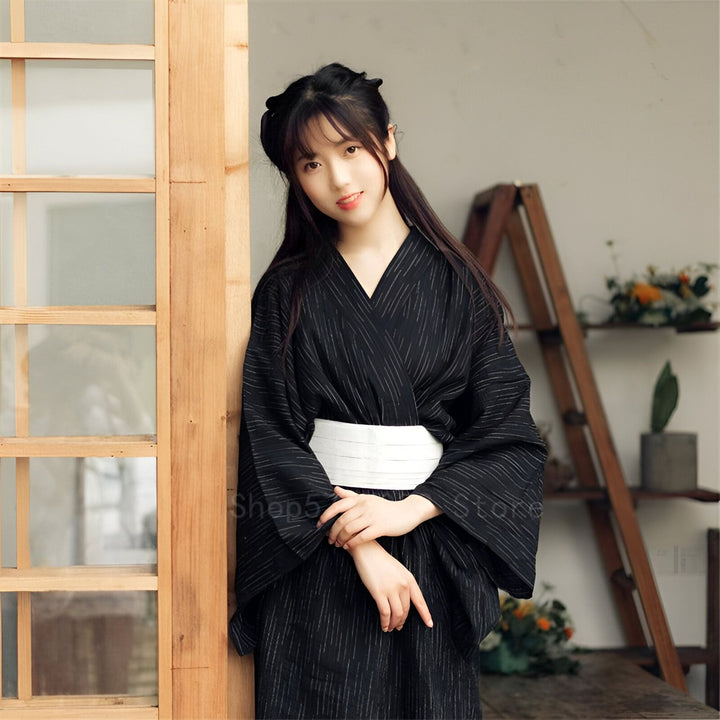 Jeune femme portant un kimono noir traditionnel avec une ceinture blanche. Kimonos disponibles à la vente.