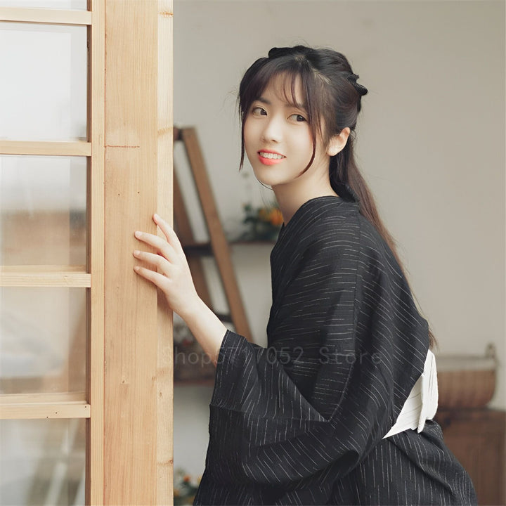 Jeune femme souriante portant un kimono noir à rayures. Kimonos traditionnels et modernes à découvrir.