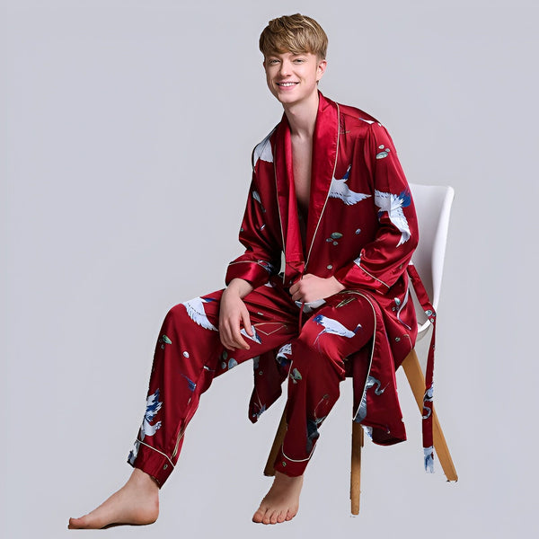 Homme souriant portant un kimono bordeaux imprimé avec des grues blanches, assis sur une chaise. Vêtements de détente élégants, collection kimono pour hommes.