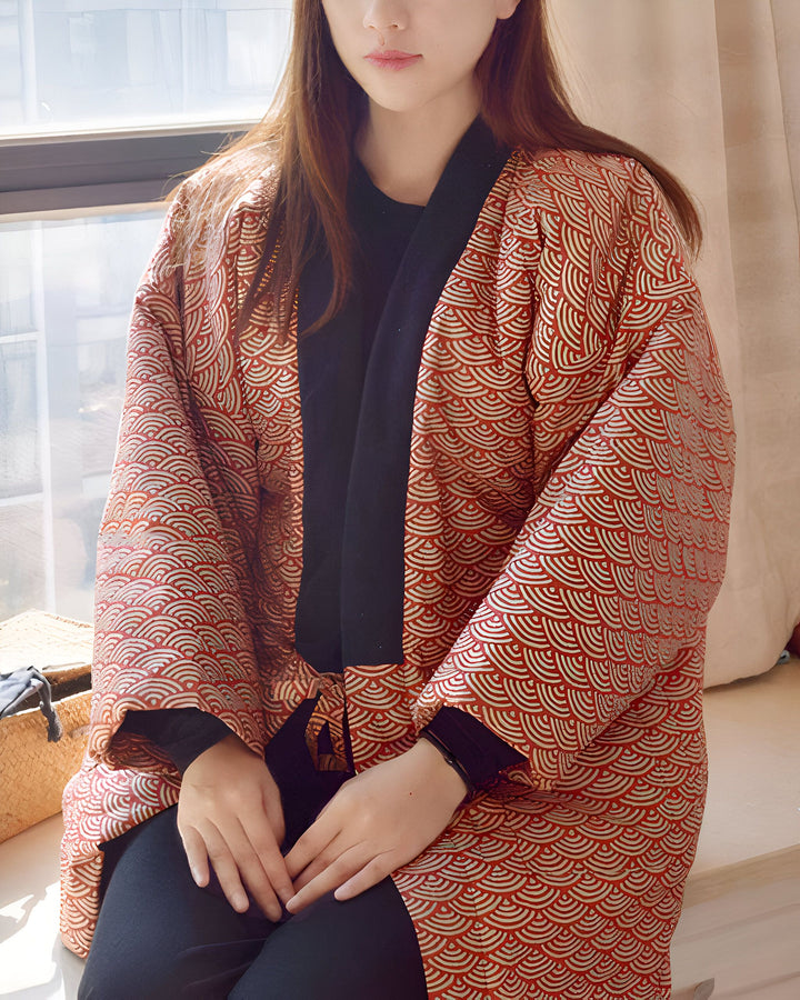 Femme assise près d'une fenêtre, portant un kimono rouge et or avec des motifs japonais de vagues. Kimonos disponibles à l'achat.