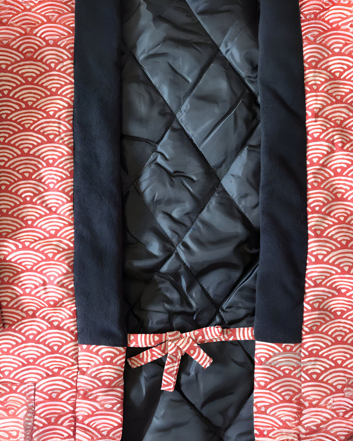 Détail d'un kimono avec motif de vagues rouges et blanches, bordure noire et doublure matelassée noire. Un ruban rouge et blanc noué ajoute une touche élégante. Kimono à vendre.